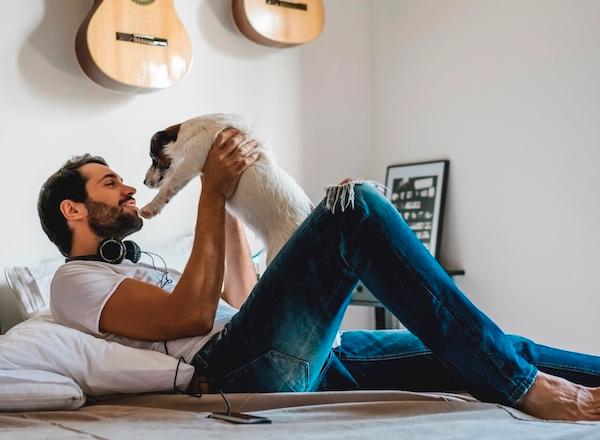 A man laying on a bed smiling and holding up a dog.